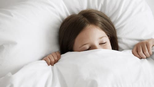 Ein junges Mädchen liegt halb bedeckt von einer Daunendecke, im Bett.